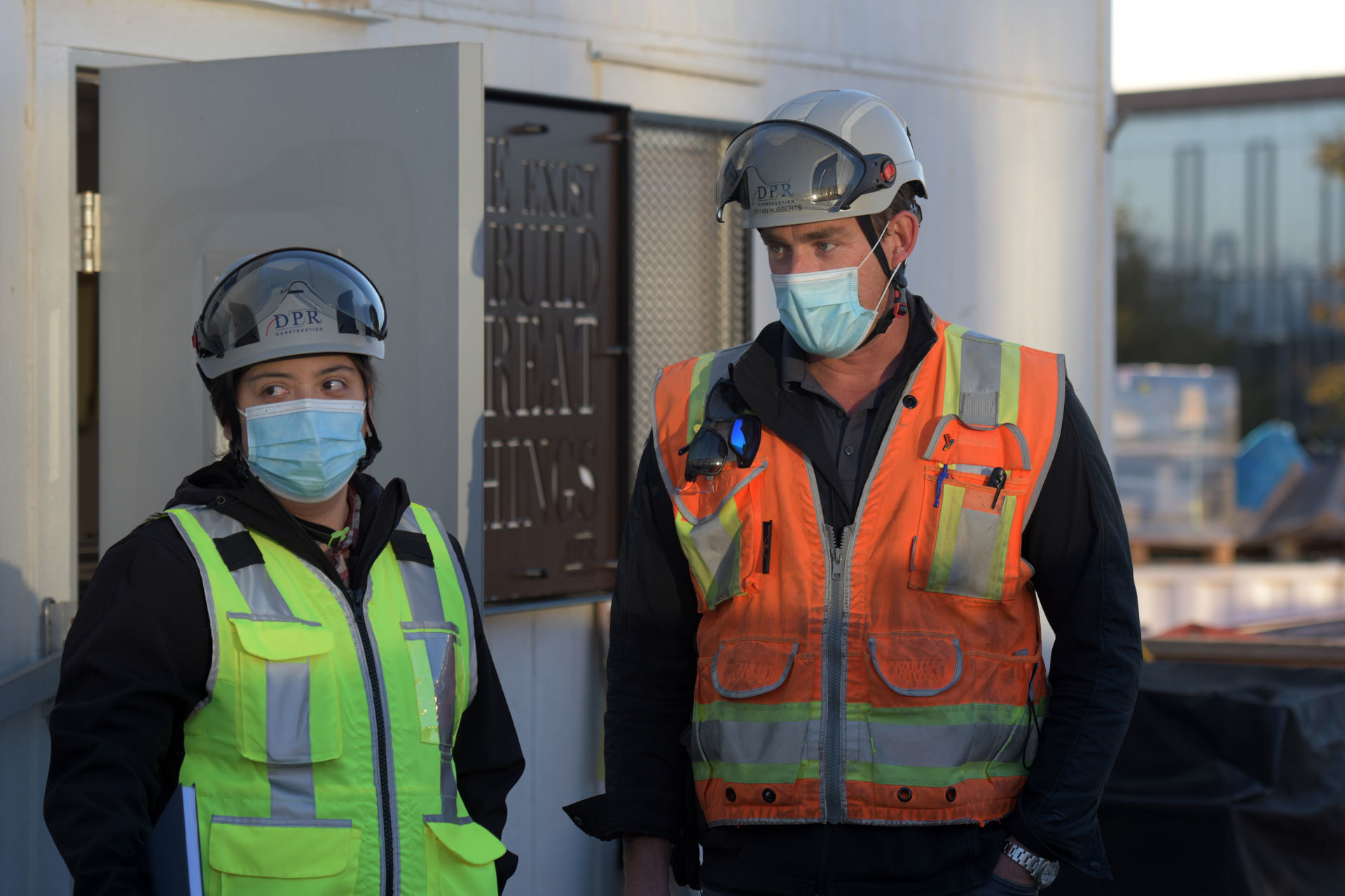 Two DPR employees in full safety gear take part in a morning meeting before the beginning of the workday.