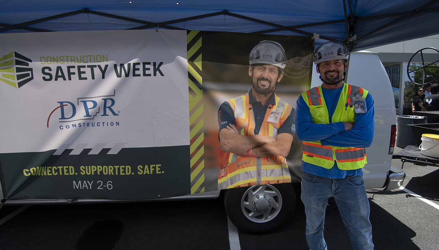 A construction worker stands next to his own image on a Construction Safety Week banner.
