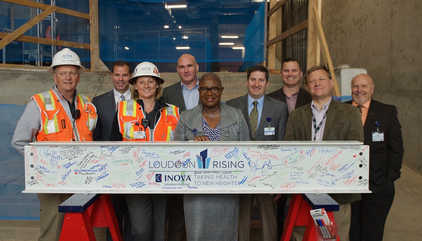 Design and construction team poses with signed beam alongside hospital CEO Deborah Addo.