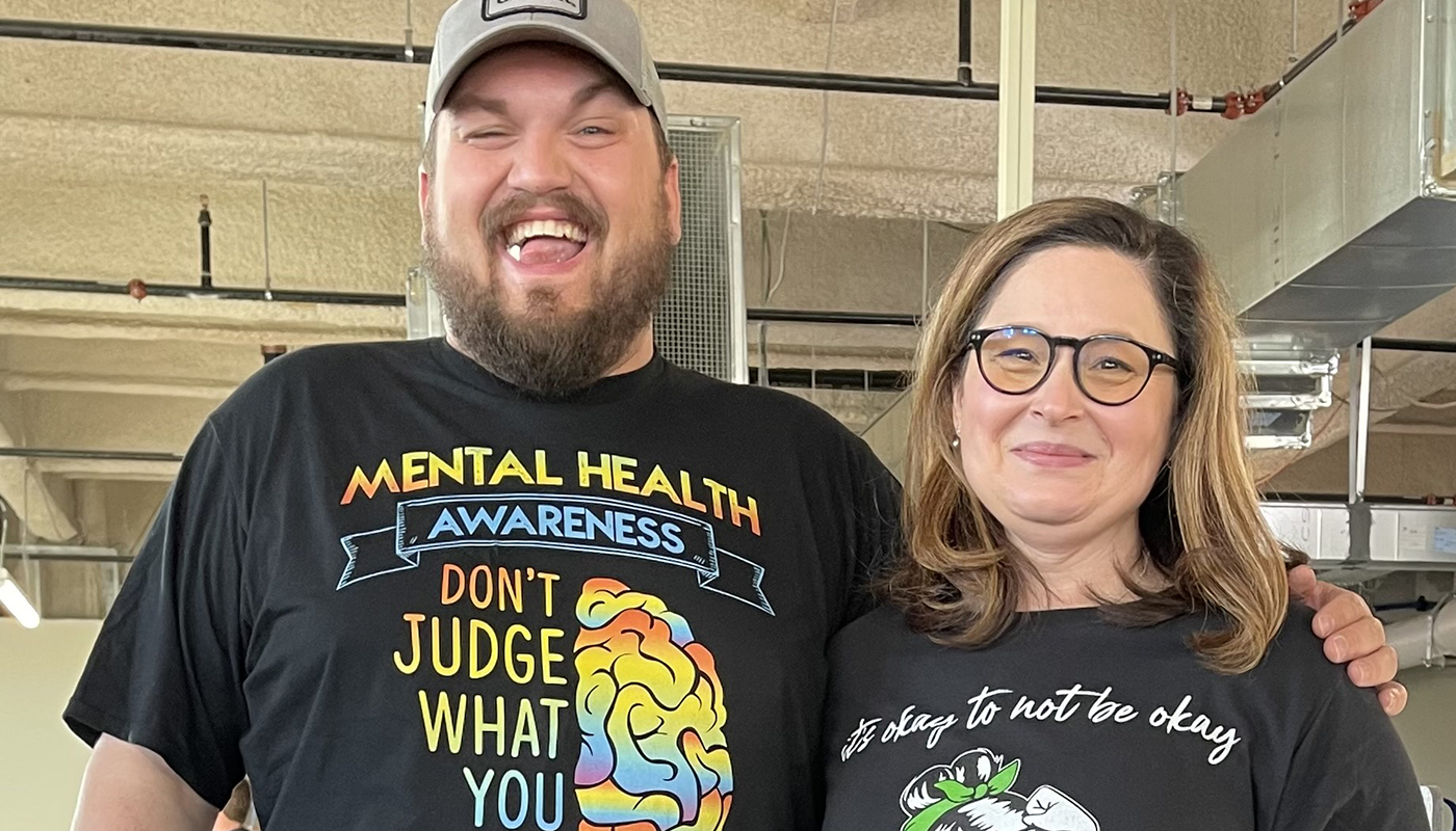 A man and a woman stand together wearing t-shirts with positive mental health messages.