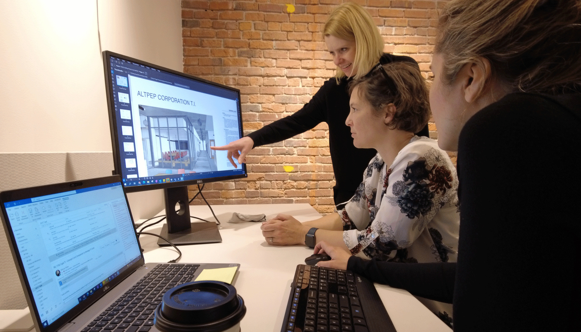 Three women huddle around computer screens showing a building model. 